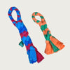 One of each size of Chelsy's Toys tug toy, side by side. These knotted, rope-style fleece toys have an integrated loop "handle", with a thicker knotted body, and loose fleece ends. Color examples are medium and dark blue with maroon for the X-Large toy, and green & orange for the small toy.