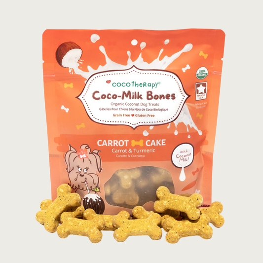 6 oz orange bag of CocoTherapy Coco-Milk Bones Carrot Cake dog treats with treats displayed in front. Made with carrot, turmeric & coconut milk. Grain-free, gluten free. USDA organic, made in USA. Treats in front of bag are orangish-tan in color and bone-shaped.