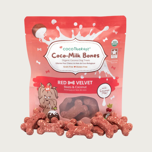 6 oz red bag of CocoTherapy Coco-Milk Bones Red Velvet dog treats with treats displayed in front. Made with beets, coconut & coconut milk. Grain-free, gluten free. USDA organic, made in USA. Treats in front of bag are reddish in color and bone-shaped.