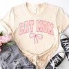 Cream colored short sleeve t-shirt with Cat Mom in large, varsity style lettering on the chest. Border color on text is hot pink, interior text color is pastel pink with tiny floral accents. There is a hot pink bow detail placed underneath the text.