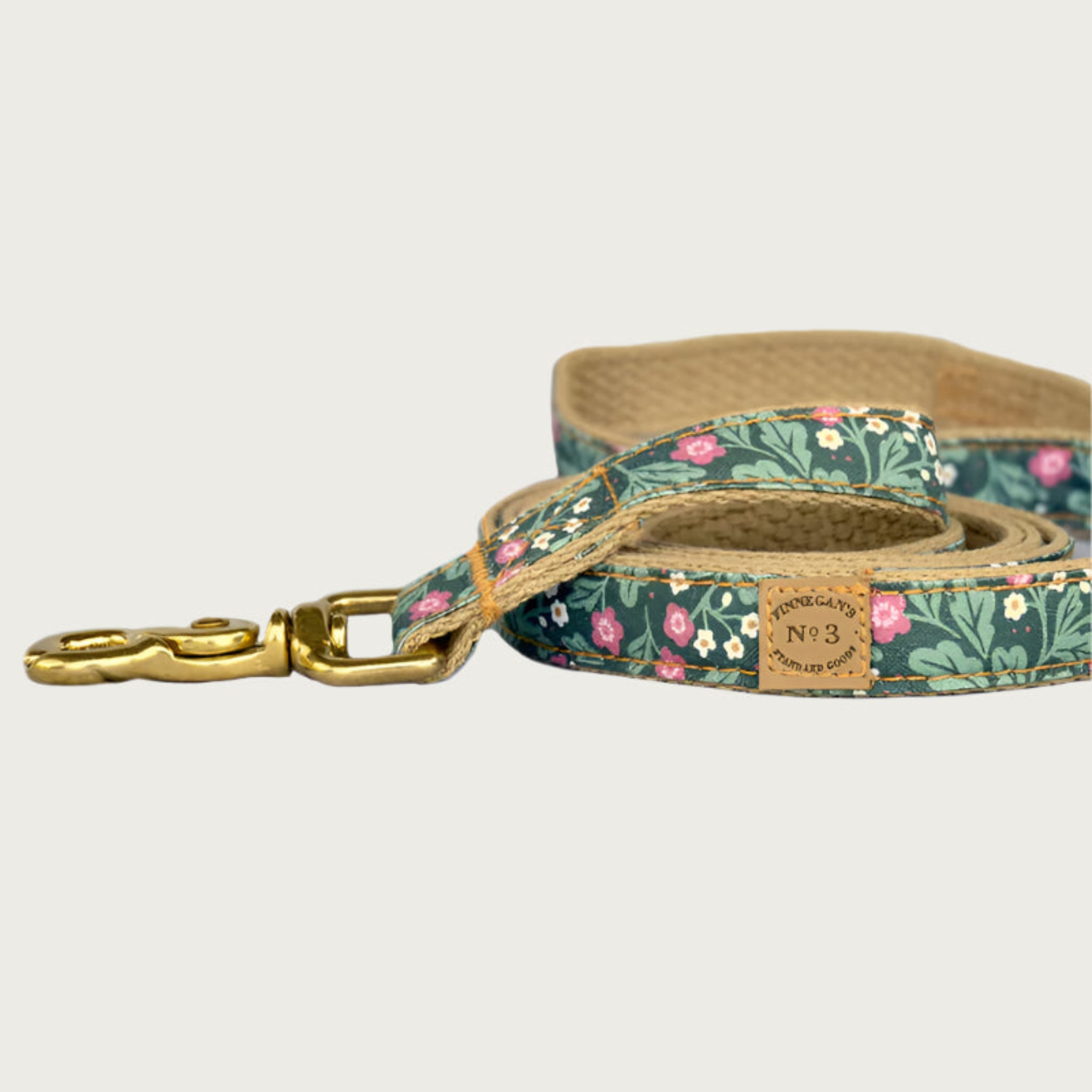 Dog leash with a botanical-themed print, in a base color of hunter green with small pink & white floral details with lighter green leaves. Brass clasp.