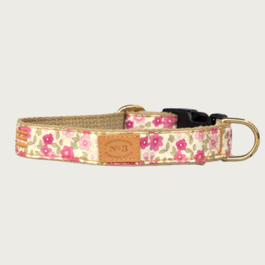 Dog collar with a multi-toned pink floral pattern on a pale yellow background, with a brass D-ring and black plastic buckle.