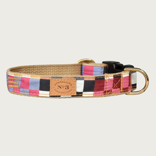 Dog collar with an uneven, checkered pattern, formed by blocks of different checkered color combinations; pink/lavender, black/white, burgundy/pink, yellow/white, and more. Has a tan cotton underside, brass hardware and black plastic buckle.