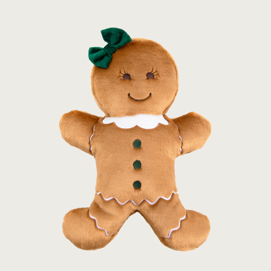 Plush gingerbread girl dog toy, wearing a green bow on her head, with embroidered details (smiley face, green buttons down belly, white ruffled collar, and white icing details on arms & legs.)
