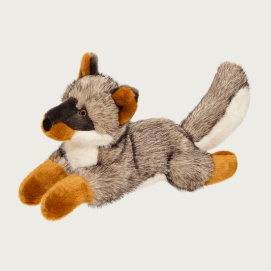 Plush fox dog toy, laying on its stomach with outstretched legs. It is covered in fluffy, faux fur beige plush with black on tips to look more like real fox fur. Its chest, snout, ears and tail are accented with either cream, black or tan faux fur plush.