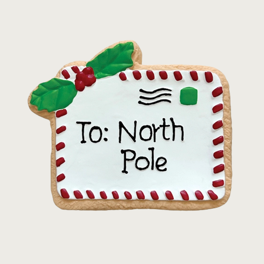 Flat, latex dog toy decorated to look like a sugar cookie. It's shaped like a white envelope with red "stitching" on the edges, holly in the top left corner, and it reads "To: North Pole".