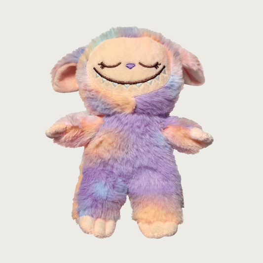 Plush dog toy designed to look like one of the popular Labubu collectible toys. It has a wide toothy grin, and features shades of peach, purple, and other tie-dyed pastel colors.