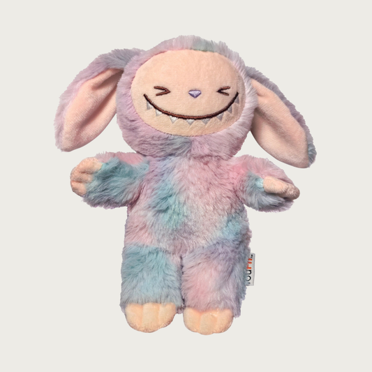 Plush dog toy designed to look like one of the popular Labubu collectible toys. It has floppy ears, a wide toothy grin, and features muted pastel tie-dye colors.