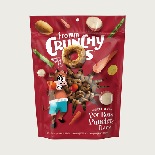 A deep red pouch of Fromm Crunchy O's 'Pot Roast Punchers' flavor dog treats, featuring cartoon graphics of a cow wearing boxing gear and vegetables, with a clear window showing the treats inside.