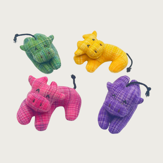 Four small woven cotton cow-shaped cat toys in green, yellow, pink, and purple. Two have a curved shape, and two are laying flat with outstretched legs.