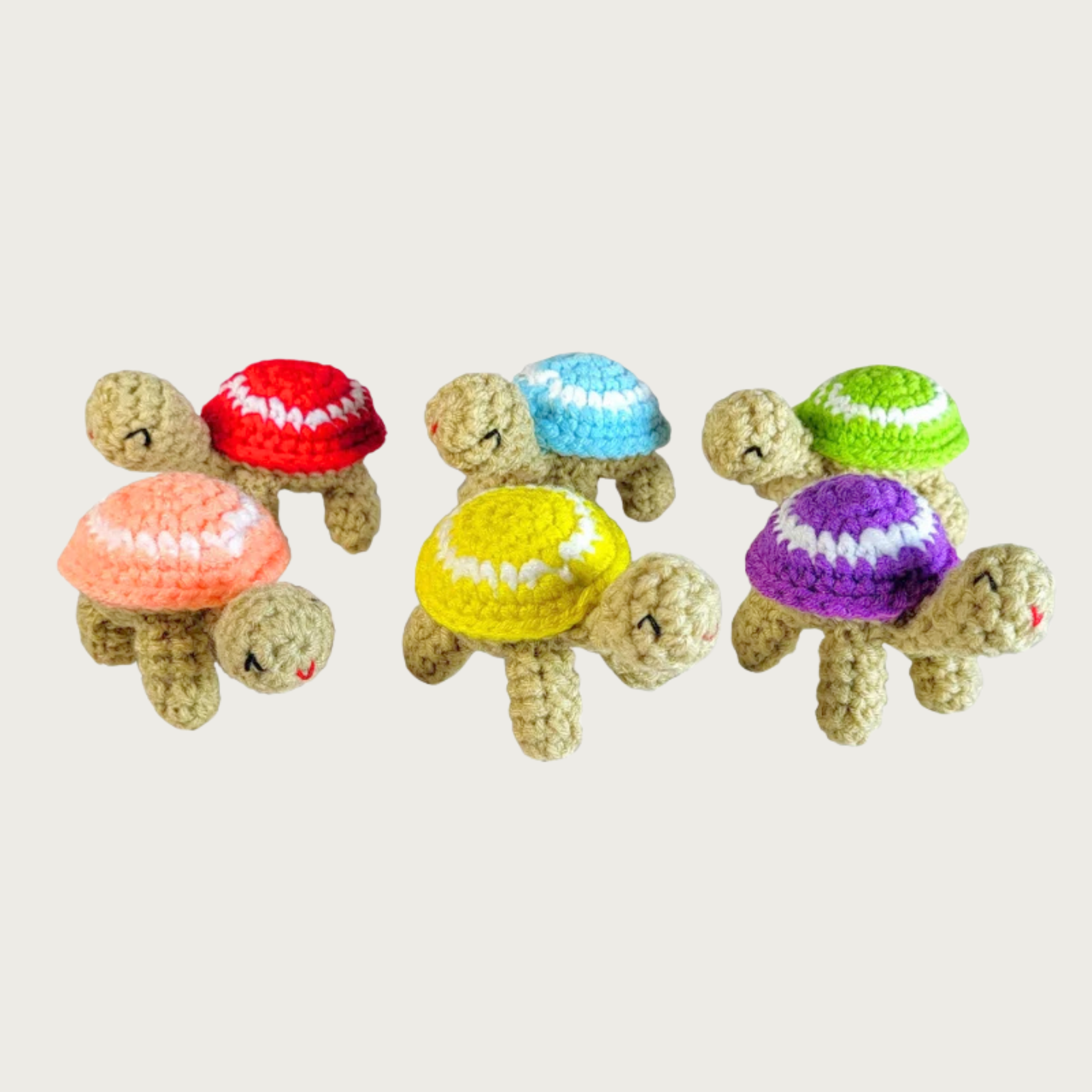 Six crocheted turtle-shaped cat toys arranged in two rows. The turtles have beige bodies and shells in various colors including red, light blue, yellow, purple, green, and peach, with a white circle on their shells, and embroidered facial details.