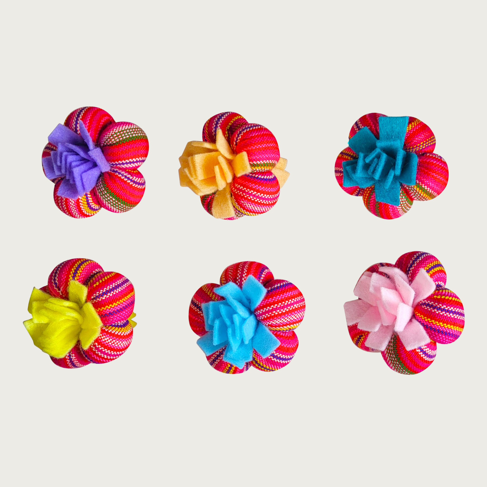 Six brightly colored Lili Paddi cat toys arranged in two rows. Each single toy looks like a cluster of 5 small balls. Each one features a striped red, pink, yellow and purple base with a different solid-colored felt ribbon accent in the center, in either purple, yellow, teal, green, blue, or pink.