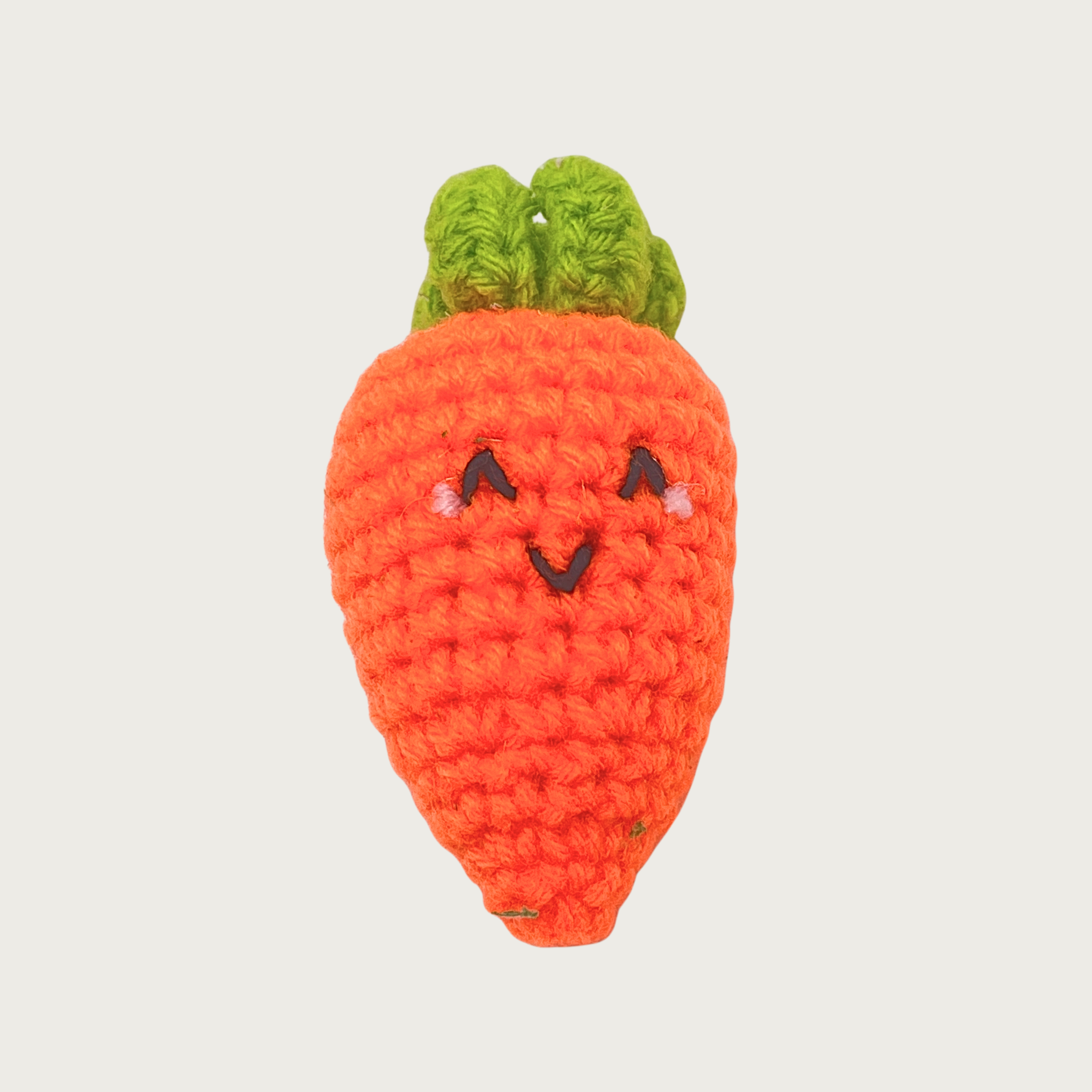 A crocheted carrot cat toy with a green leafy top, bright orange body, and an embroidered smiling face.