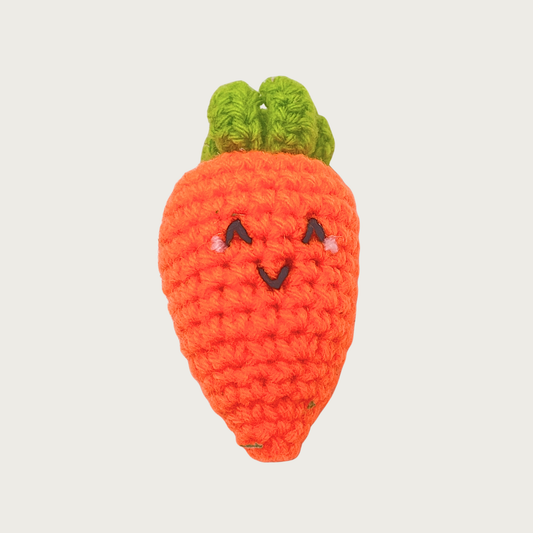 A crocheted carrot cat toy with a green leafy top, bright orange body, and an embroidered smiling face.