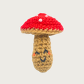 Load image into Gallery viewer, A crocheted mushroom cat toy with a red cap with white spots, and a tan stem with an embroidered smiling face on it.
