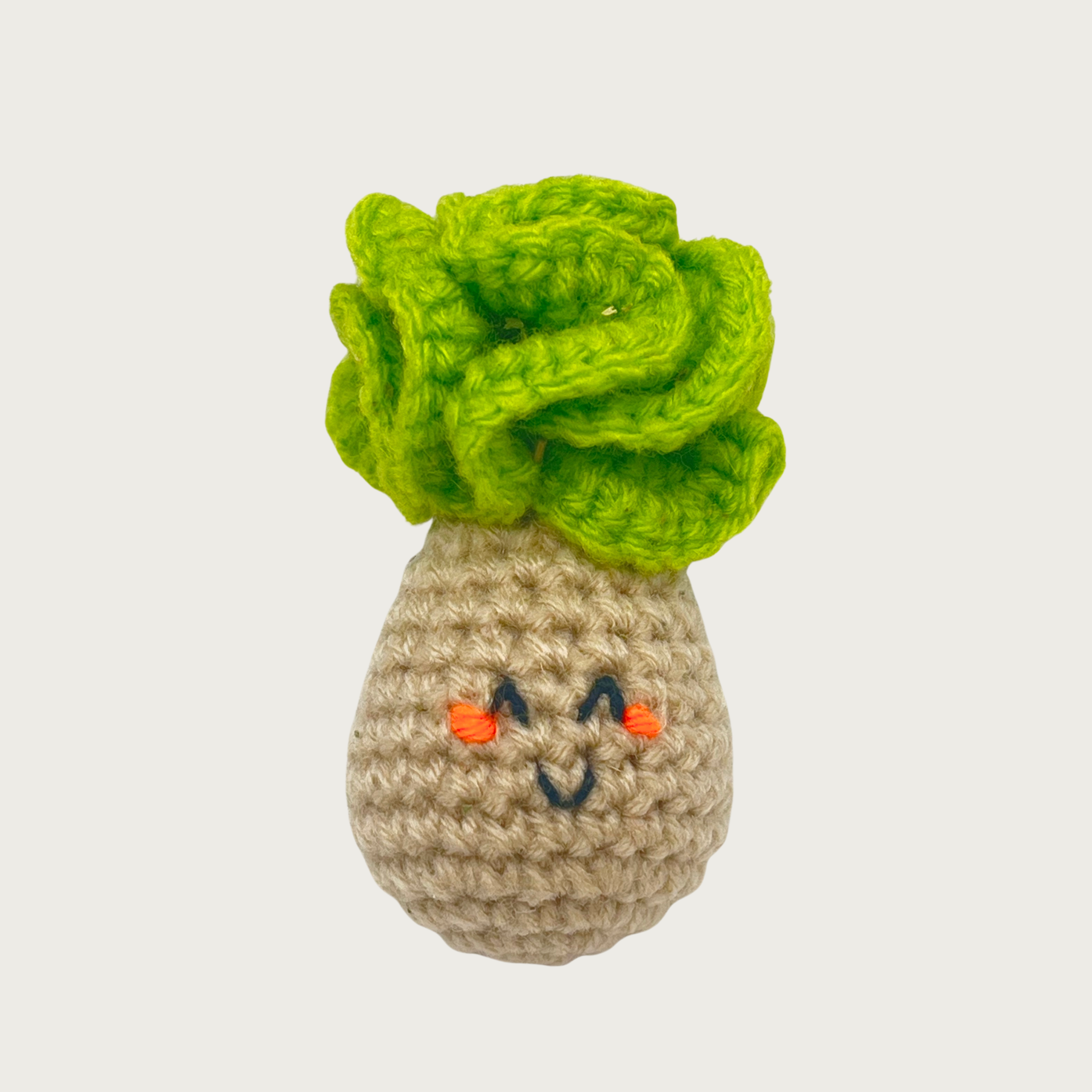 A crocheted turnip cat toy with a bright green leafy top, bulbous beige textured body, and embroidered smiling face.