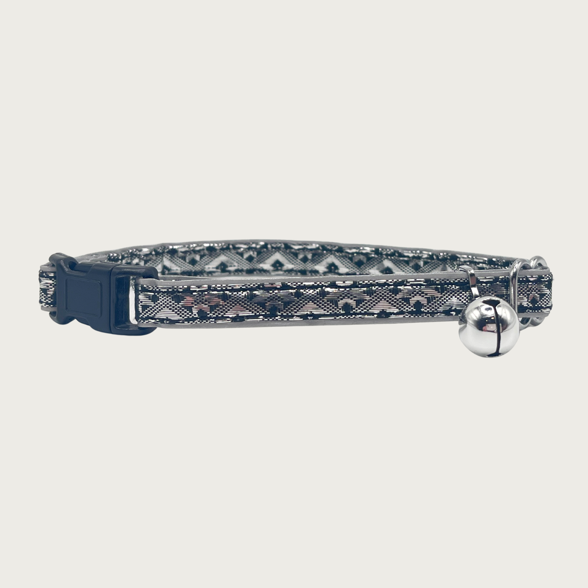 A black and silver, geometric patterned cat collar with a small silver bell and black buckle.