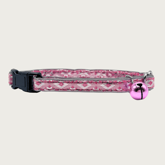 A bubblegum pink and silver, geometric patterned cat collar with a small bubblegum pink bell and black buckle.