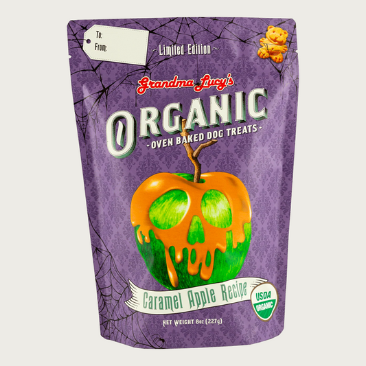 Purple bag of limited edition Grandma Lucy's Organic Oven Baked Dog Treats, Caramel Apple Recipe. USDA Organic. Center illustration is of a green apple with caramel dripping down it, in the shape of a jack-o-lantern. 