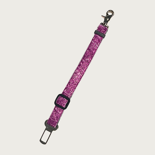 Dog seat belt in a bright, deep pink glitter nylon fabric with black nylon backing, black plastic adjustable slider and silver metal seat belt connector and harness clip.