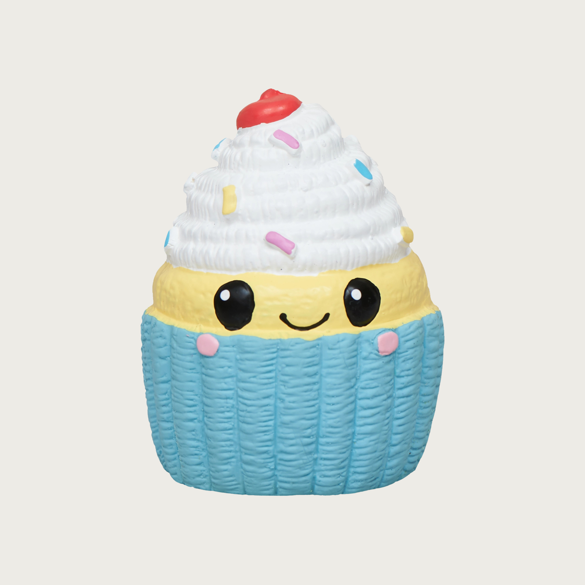 Mini latex cupcake dog toy. It has a light blue base, with strip of pale yellow "cake" above it, with white frosting on top. It has multi-colored sprinkles on the frosting, with a red cherry on top, and sweet, simple, smiley face in black, centered on the front.