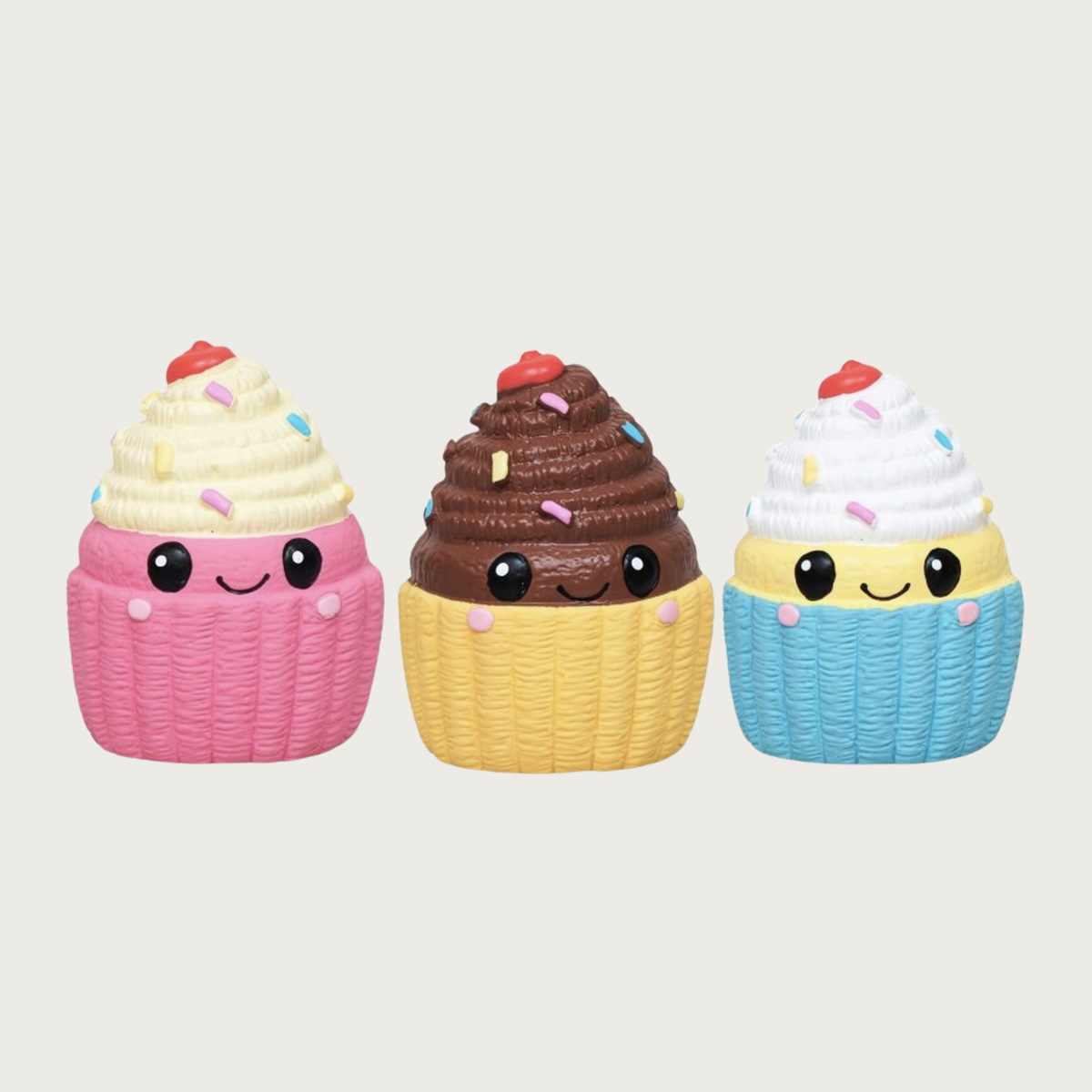 A group of three, mini cupcake shaped, latex dog toys. On the left is a pink one with vanilla frosting, in the center is a yellow one with brown frosting, and on the right is a blue one with vanilla frosting. All have multi-colored sprinkles on the frosting, with a red cherry on top, and sweet, simple, smiley faces in black, centered on their fronts.