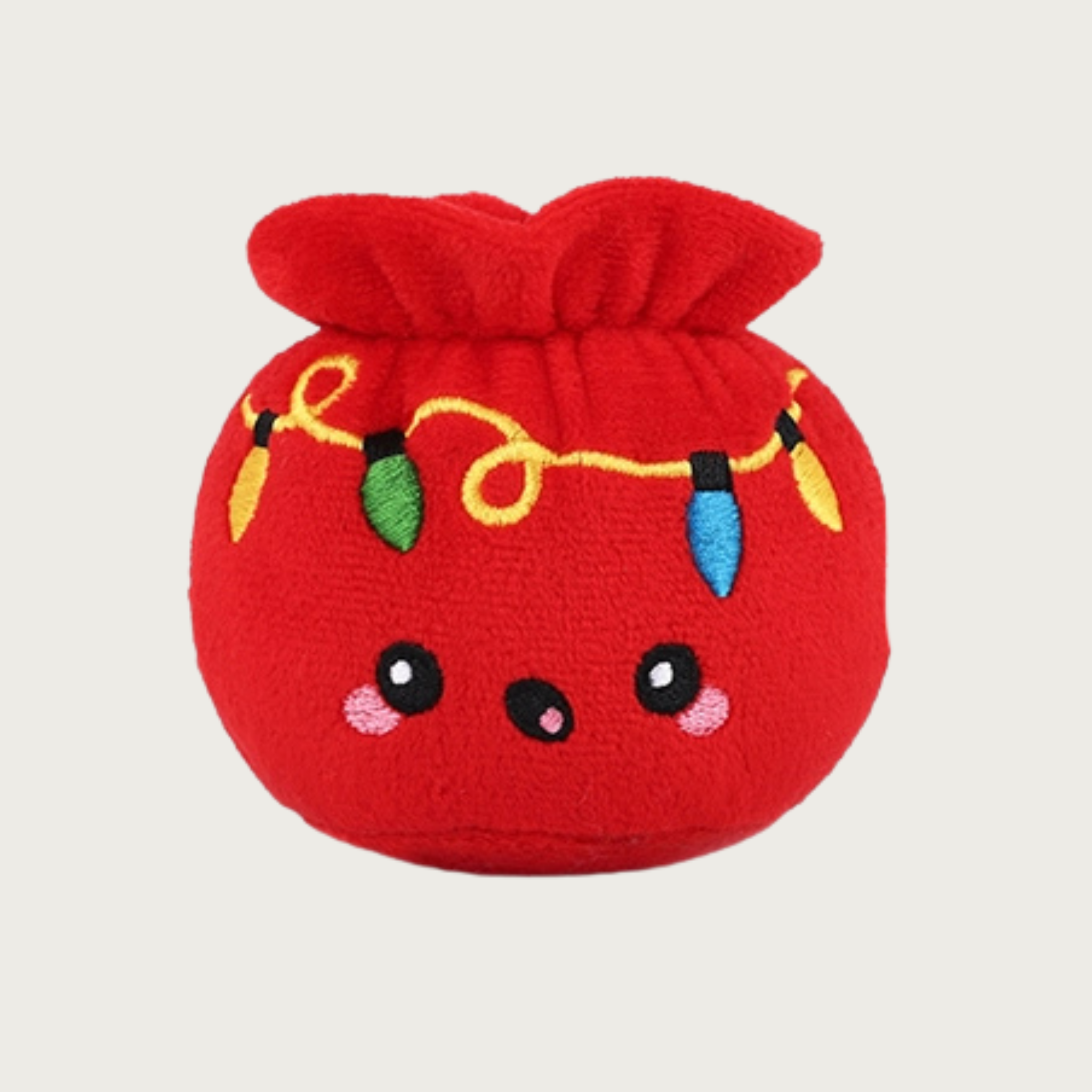 Plush dog toy in the shape of a red gift bag with embroidered holiday lights string and a cute facial expression.