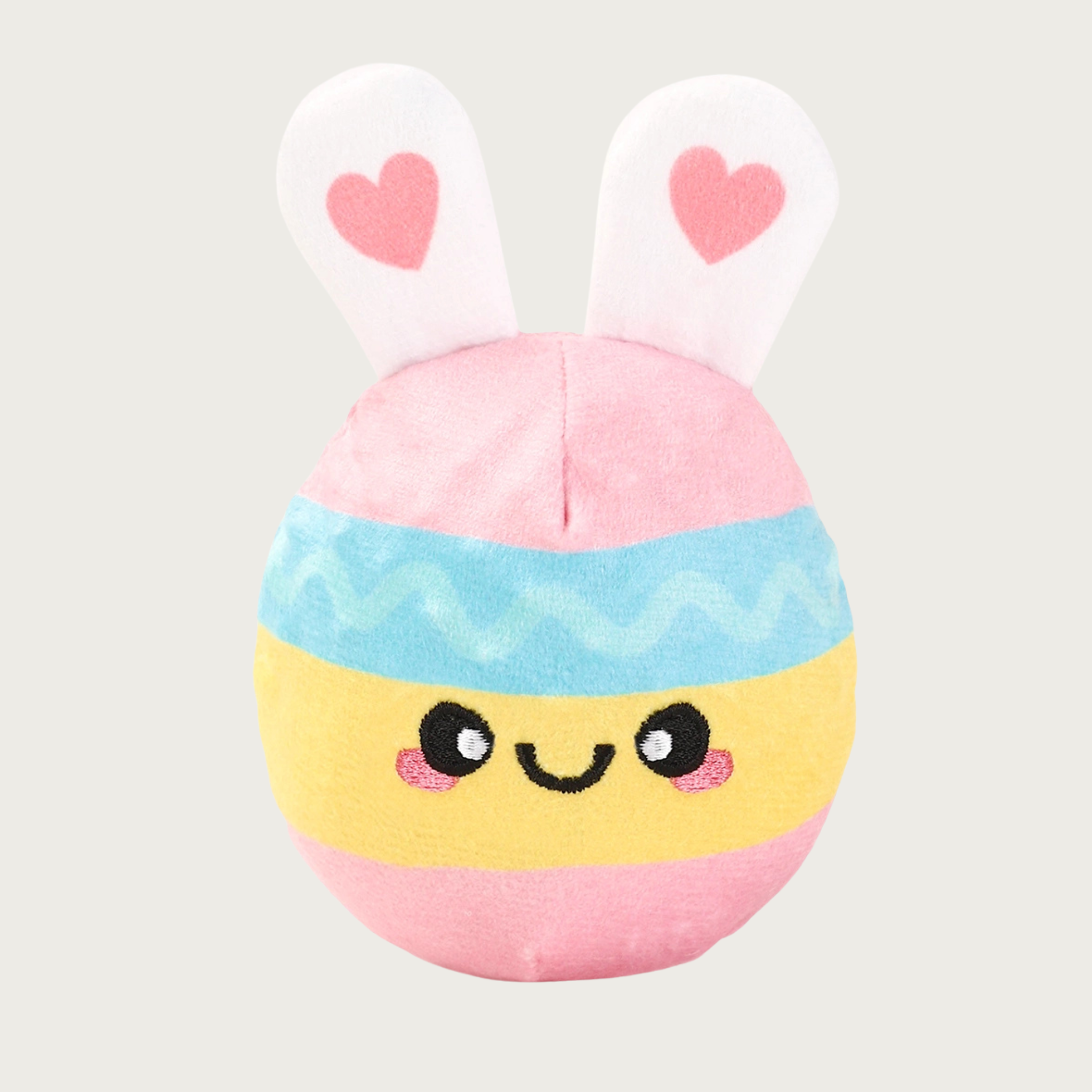 Round, plush dog toy resembling an Easter egg. Its body features horizontal pink, pale blue, and pale yellow wide stripes. It has white bunny ears with pink hearts in the center and a cute embroidered facial expression.