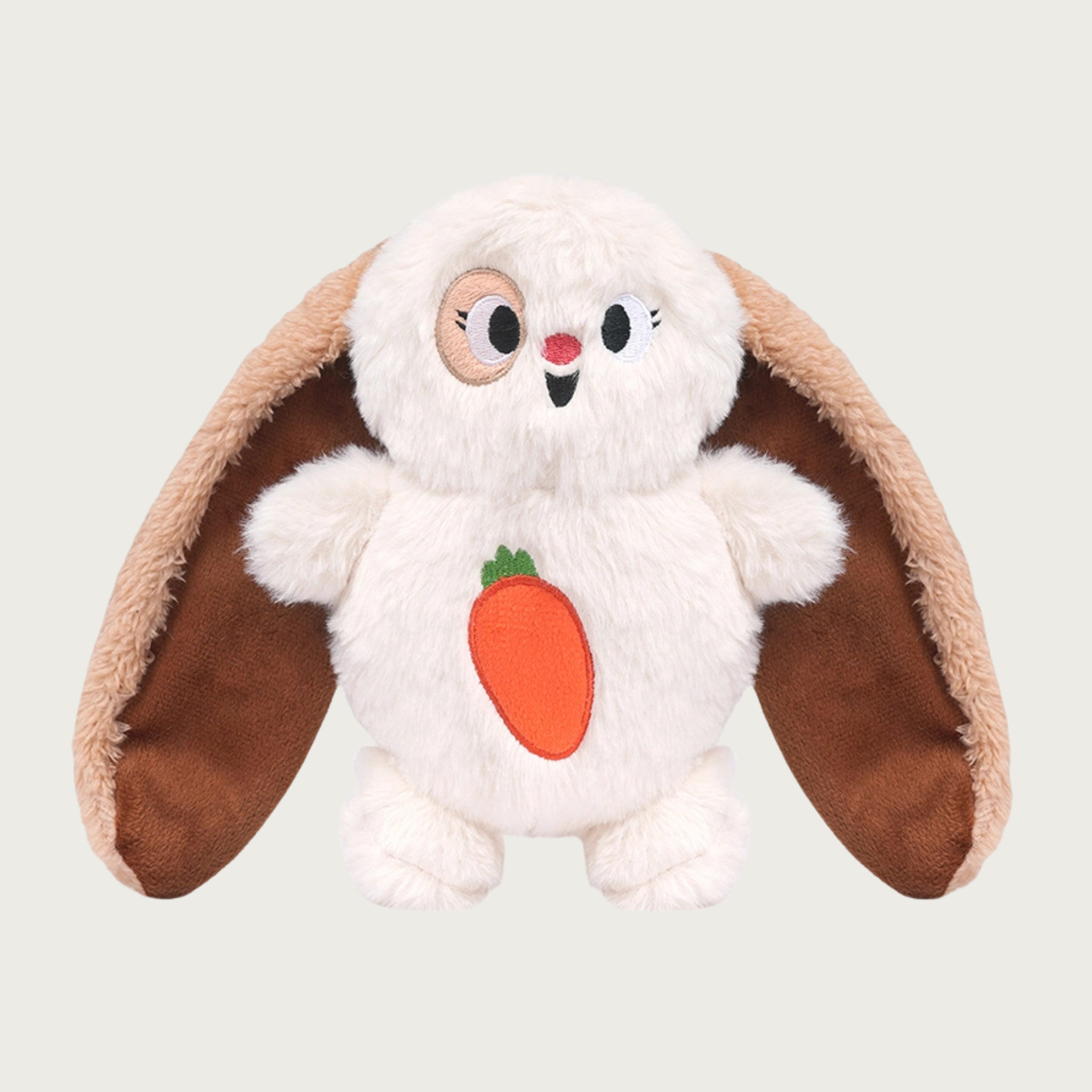 Plush dog toy shaped like a squat bunny with extra long ears. Its body is white, with long tan ears that are as long as its body. It has a carrot applique on its belly, and an embroidered smiling facial expression.