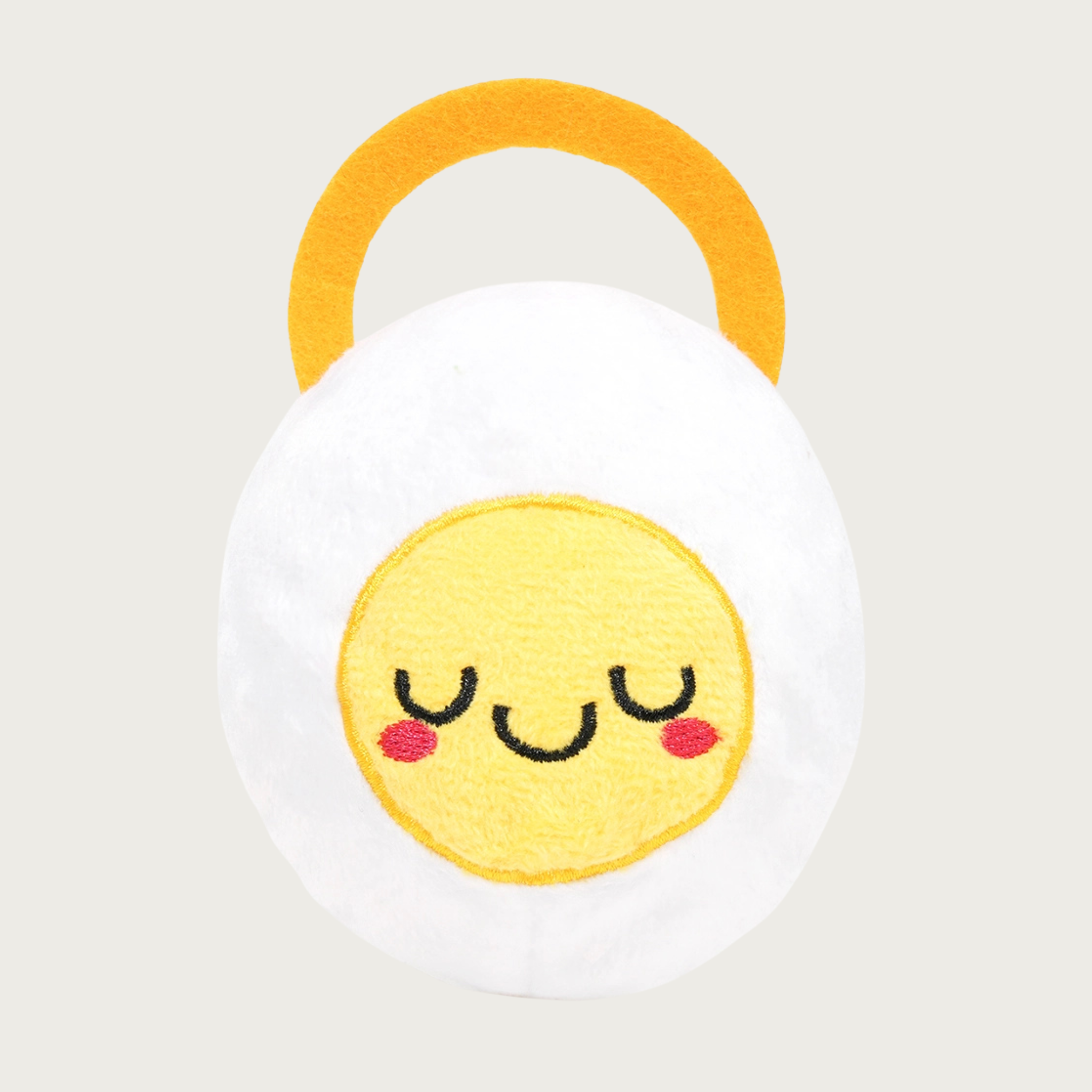 Round, plush dog toy resembling a cut hard-boiled egg with a cute embroidered facial expression. It has a gold felt ring on its back that makes it appear to be wearing a halo.