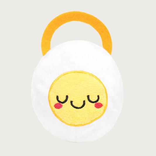 Round, plush dog toy resembling a cut hard-boiled egg with a cute embroidered facial expression. It has a gold felt ring on its back that makes it appear to be wearing a halo.