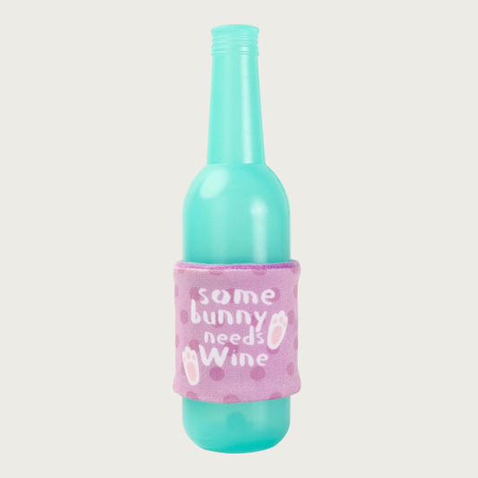 Bright aqua, rubber dog toy shaped like a wine bottle.  The removable plush sleeve is pale purple, accented with medium purple dots, and bunny feet, with text that reads, "some bunny needs wine."