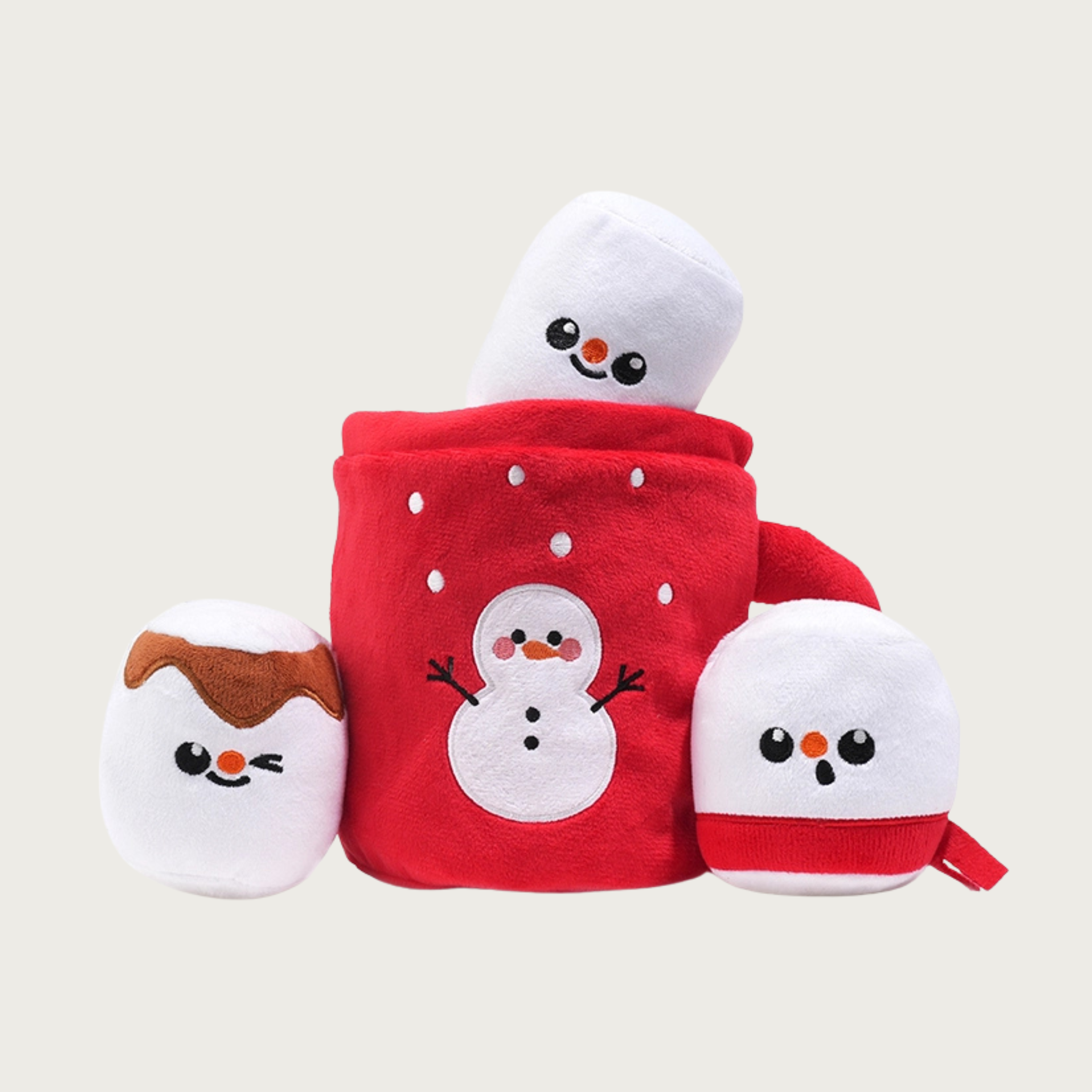 Christmas-themed plush dog toy, resembling a mug of hot cocoa with three separate, marshmallow plush toys. Each marshmallow has a different, cute embroidered expression. The mug is red with snowman detail on the front.