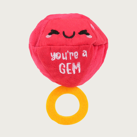 Plush dog toy designed to look like a ring with a huge jewel. The jewel is red with a sweet embroidered smile, above text that reads "You're a GEM." It is attached to a smaller, gold colored felt loop "ring".