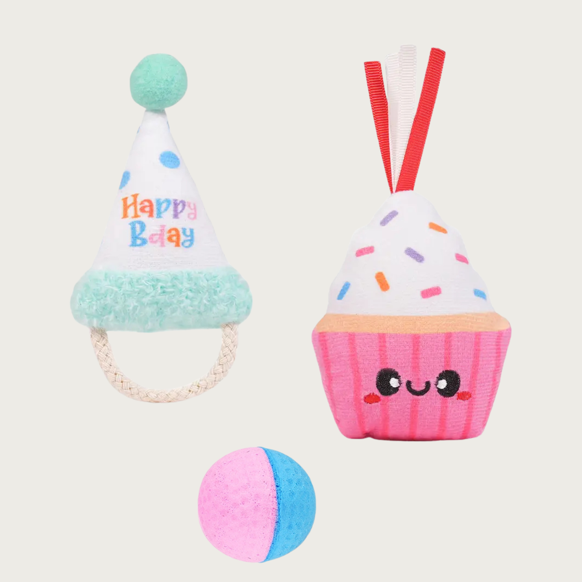 Three birthday themed cat toys. On the left is a plush party hat with seafoam green pom pom and trim, with a cotton rope "chin strap", on the right is a pink smiling plush cupcake with ribbon coming out of the top, and on the bottom is a pink & blue foam ball. 