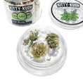 Load image into Gallery viewer, Closeup of 3 catnip buds in open, disc shaped grinder. Lid is off to see interior wide "teeth" used for grinding.
