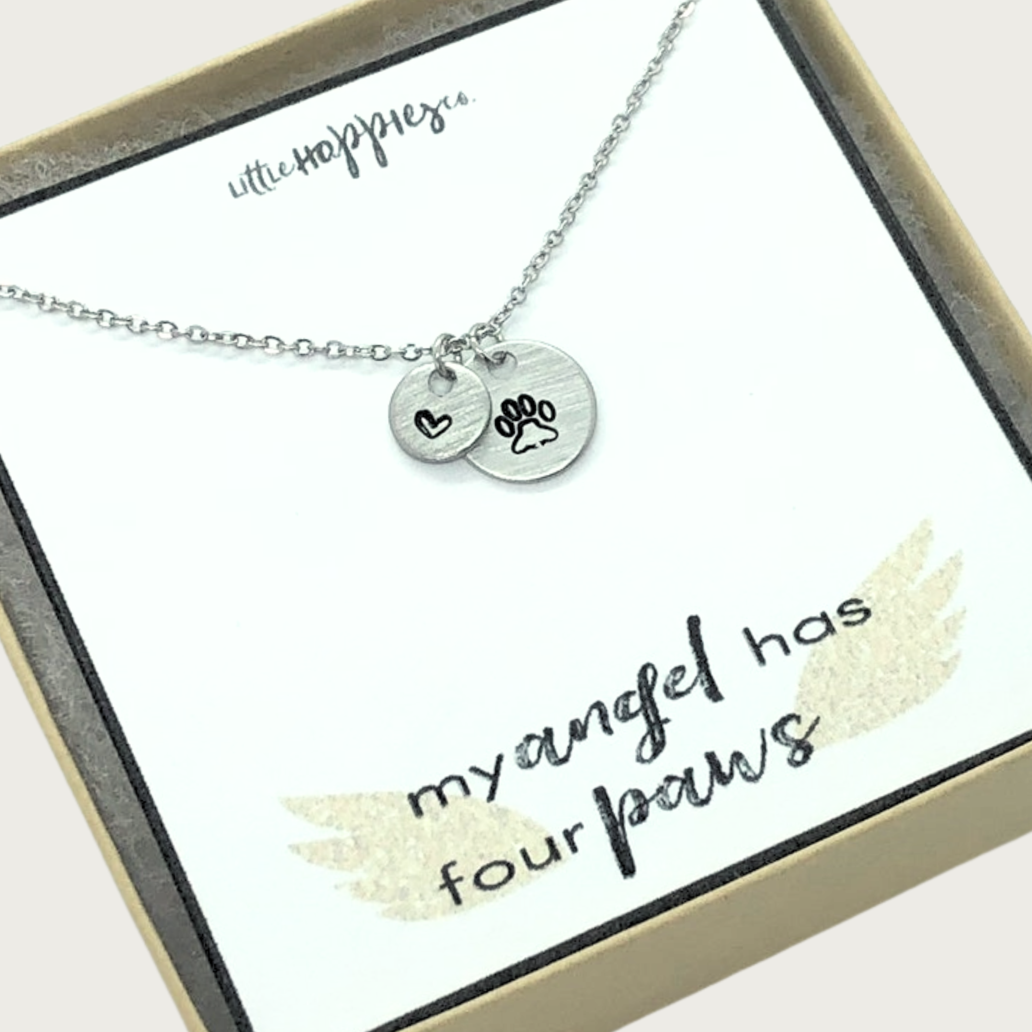 Silver-toned, delicate chain link necklace with small, round charm with outlined black paw print detail, and a smaller coordinating charm with an outlined heart. Set on white card that reads "my angel has four paws" with angel wings accent. Comes in brown gift box.