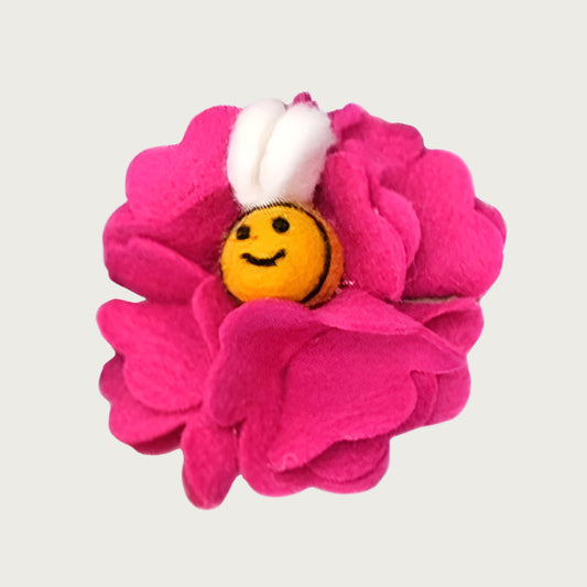 Felted wool dog collar flower, shaped like a hot pink colored hydrangea flower, with a smiling yellow bee with wings in the center.