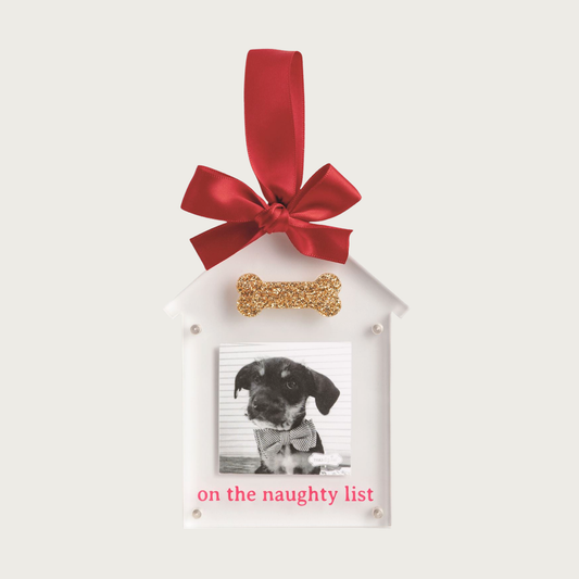 Christmas-themed, decorative white ornament with dog house shaped photo frame. Hangs from a red ribbon and features a glittery gold bone above your dog's photo. Underneath the photo, text reads 'on the naughty list' in red.