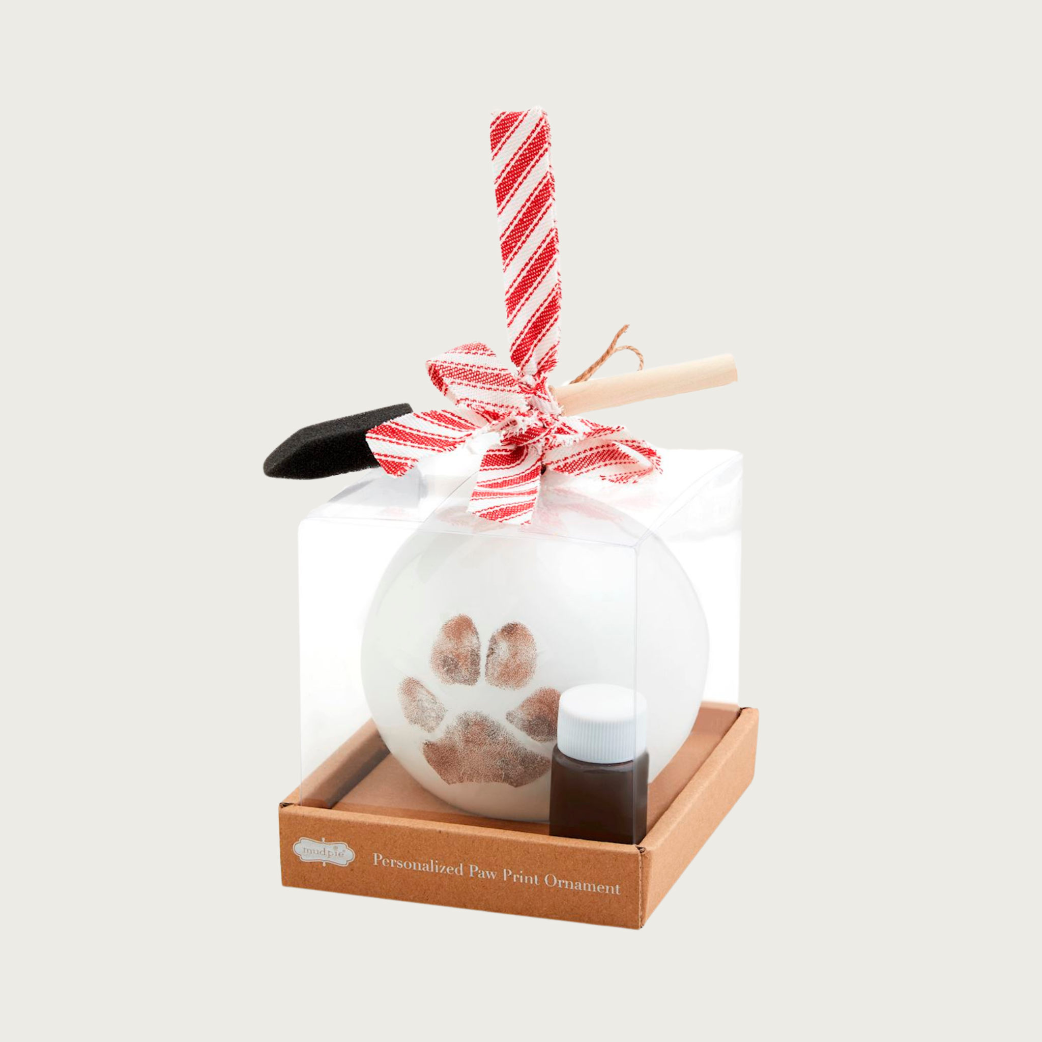 Personalized paw print ornament kit in a clear box. The round, white ornament comes with a red and white striped ribbon, paintbrush, and paint.