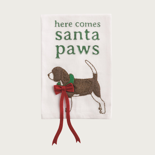 Christmas-themed white decorative towel, with a beagle-type dog wearing a long, deep red bow that trails off the bottom of the towel. Green text on top reads: "Here comes Santa Paws".