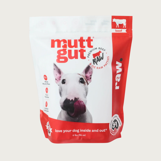A 6 lb bag of Mutt Gut raw beef dog food, featuring a white and red stand-up, resealable bag with a picture of a Bull Terrier on the front. Text called out in red circles on the left side of the bag reads: 90% whole muscle meats 8% organic vegetables, 2% BiomePet & Minerals. 6 lbs.