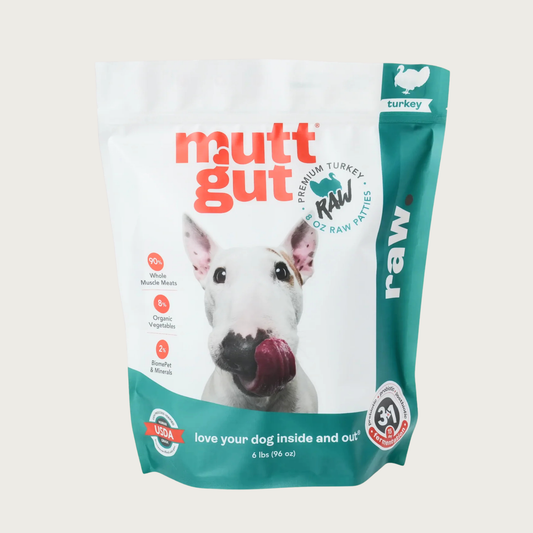 A 6 lb bag of Mutt Gut raw turkey dog food, featuring a white and teal stand-up, resealable bag with a picture of a Bull Terrier on the front. Text called out in red circles on the left side of the bag reads: 90% whole muscle meats 8% organic vegetables, 2% BiomePet & Minerals. 6 lbs.