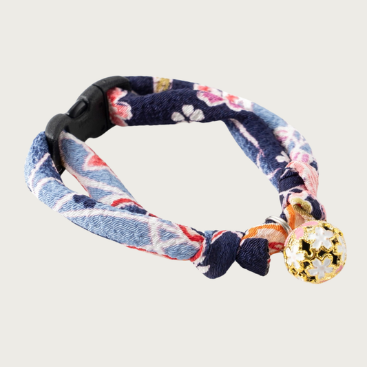 Cat collar with a navy blue, light blue, pink & coral Asian-inspired floral print. Each knotted end has a loop for adjusting the collar's size up or down. A round gold charm is attached, with enameled cherry blossom motif in cream & pink.