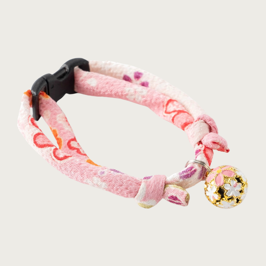 Cat collar with a pink, coral & purple Asian-inspired floral print. Each knotted end has a loop for adjusting the collar's size up or down. A round gold charm is attached, with enameled cherry blossom motif in cream & pink.