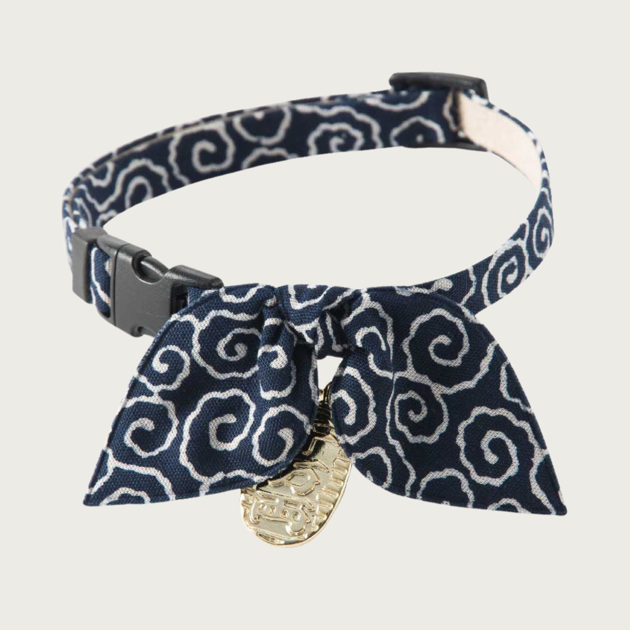 Cat collar with a dark navy blue background and white curly-q pattern, with a simple bow in the same pattern. It has a dangling gold tone Asian-inspired charm and black plastic clip & slider.