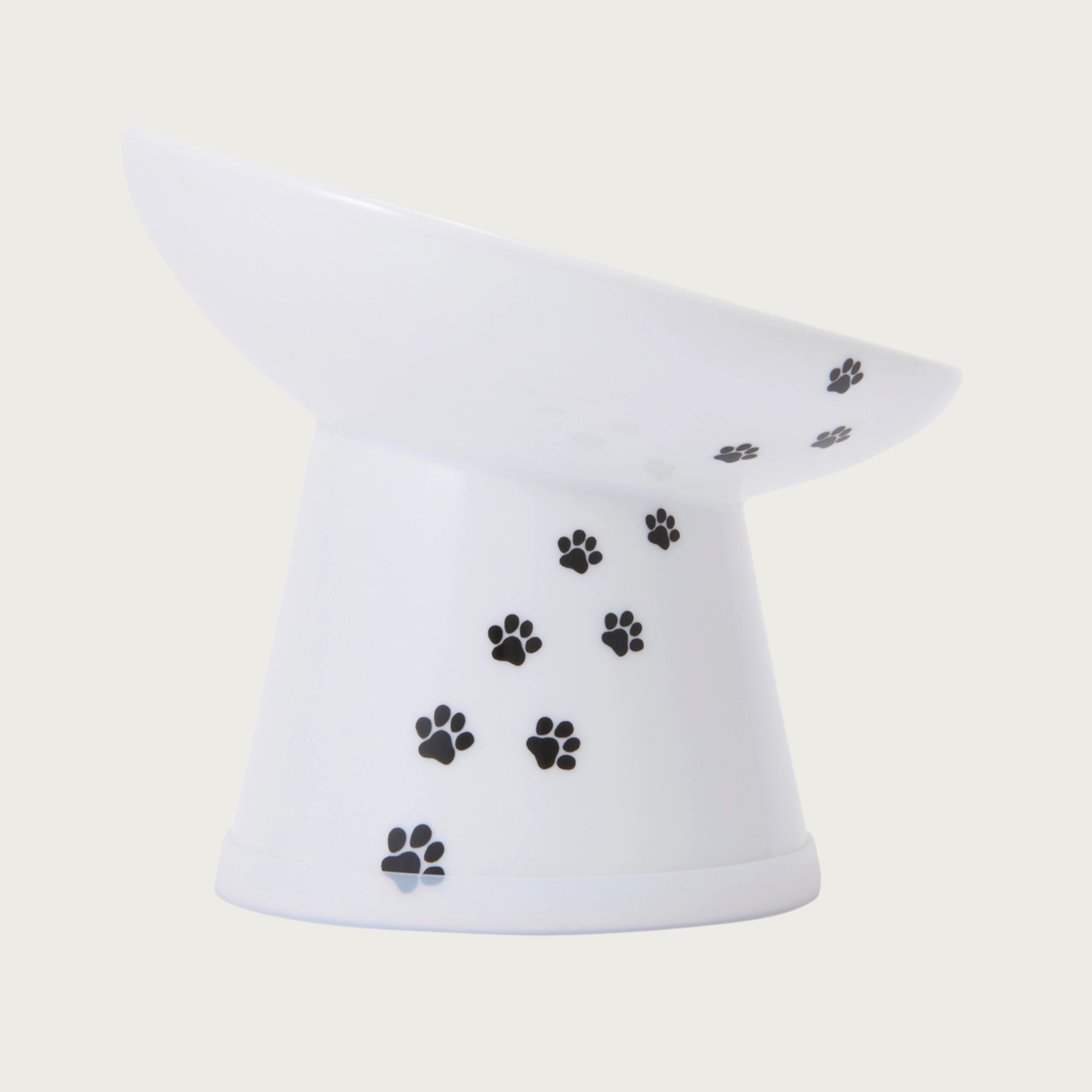 Side view of the tilted, raised, white porcelain cat food bowl with black paw print design trailing up the side. 
