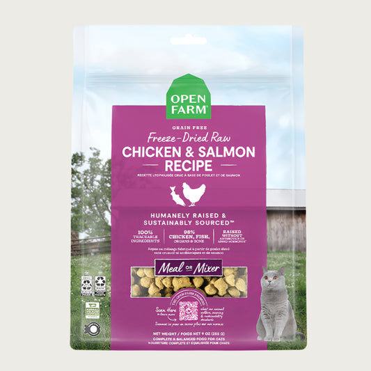 A 9 oz bag of Grain Free, Open Farm Freeze-Dried-Raw Chicken & Salmon Recipe cat food. Meal or Mixer, Humanely raised and sustainably sourced. A photo of a gray cat standing in a field on a farm covers the bag, with a magenta bar in the center to highlight the white text over it.