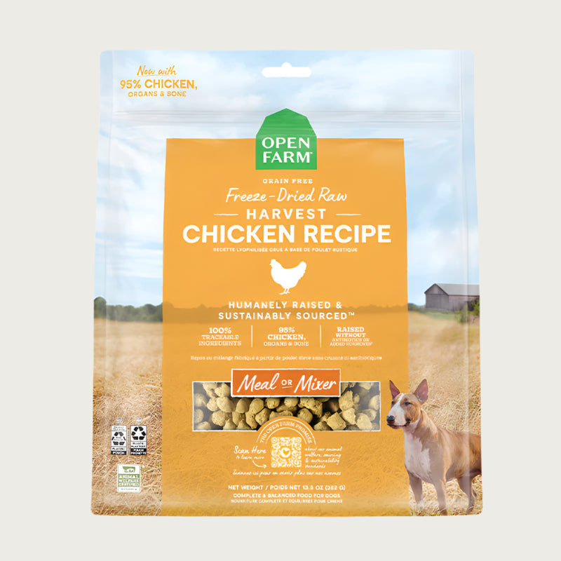 A 13.5 oz bag of Grain Free, Open Farm Freeze-Dried-Raw Harvest Chicken Recipe dog food. Meal or Mixer, Humanely raised and sustainably sourced. A photo of a Bull Terrier dog standing in a field on a farm covers the bag, with a yellow bar in the center to highlight the white text over it.