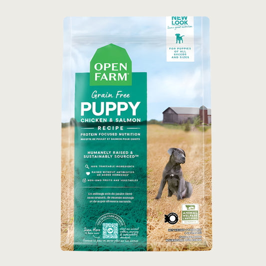 A bag of Open Farm Grain Free Puppy Recipe dog food. Humanely raised and sustainably sourced. A photo of a gray Pit Bull puppy standing in a field on a farm covers the bag, with a green bar behind the white text to highlight it.
